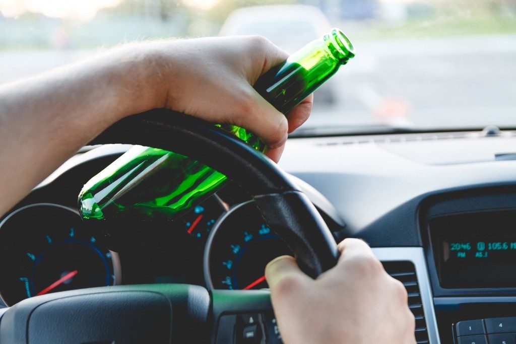 man driving while holding a bottle